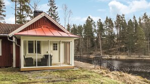 En stuga med ett rött tak, en glasdörr och utsikt över en sjö som omges av träd.