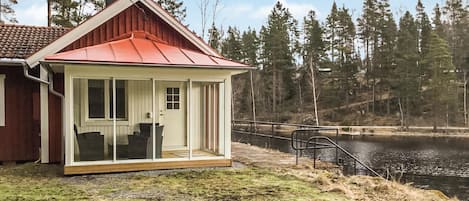 A cabin with a red roof, a glass door, and a view of a lake surrounded by trees.