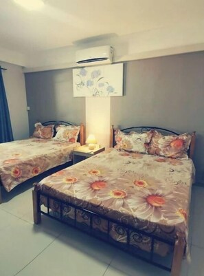A bedroom with two single beds, a nightstand with a lamp, and an air conditioning unit on the wall.