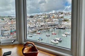 A view through a window of a harbor with boats, a town, and a wooden basket on the windowsill.