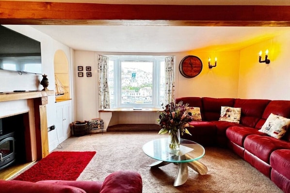 A living room with a red sofa, a glass coffee table, a fireplace, and a window with curtains.