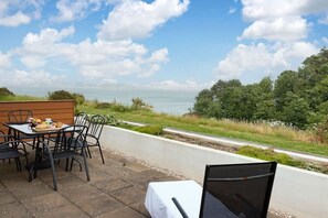Une terrasse avec une table et des chaises, donnant sur une étendue d’eau et une zone verdoyante.