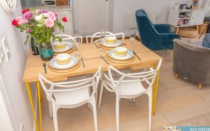 A dining area with a wooden table set for six, white chairs, and a vase of flowers. - Plover 2 - The Cove (The Cove)