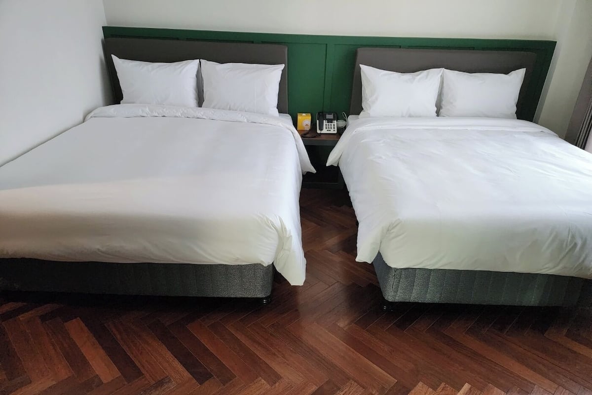 Two single beds with white linens, wooden flooring, and a green headboard.