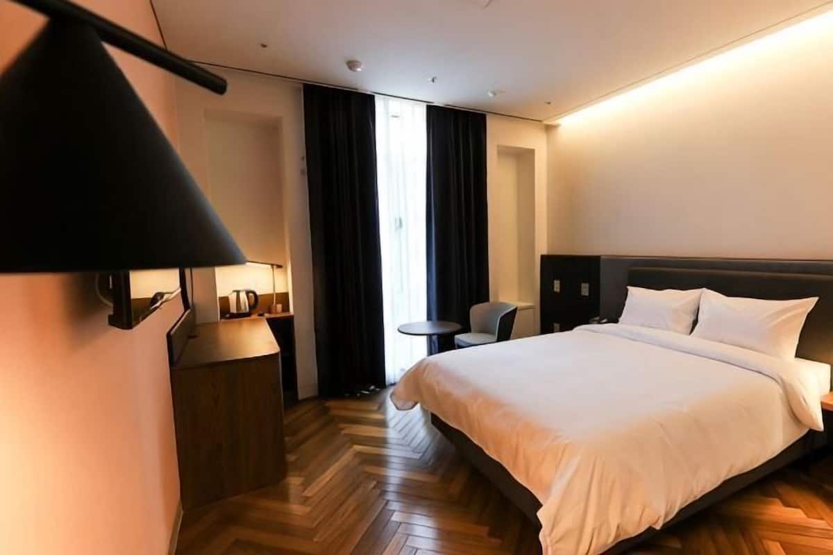 A hotel room with a bed, bedside table, lamp, chair, and a small round table.