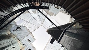 Un atrium moderne en verre, doté d’un plafond au design géométrique et de surfaces réfléchissantes.