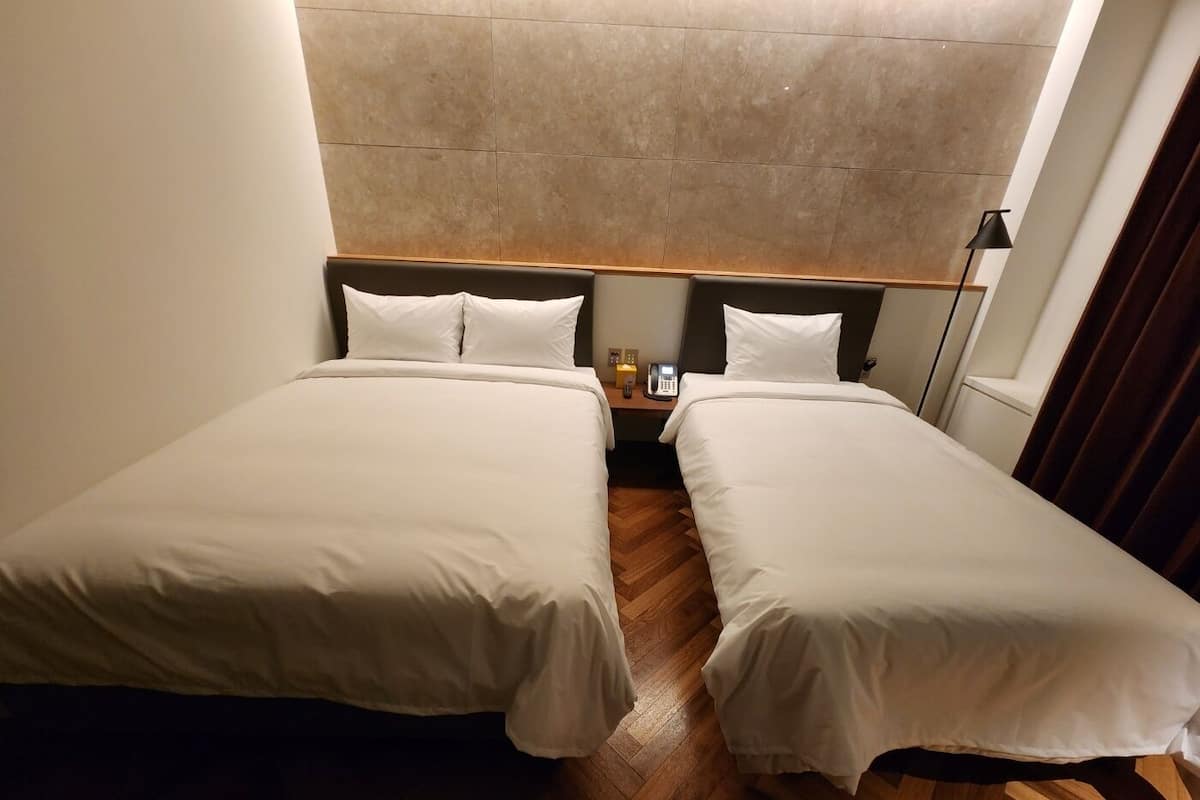 A hotel room with two single beds, a wooden floor, a headboard, a bedside table with a phone, and a lamp.