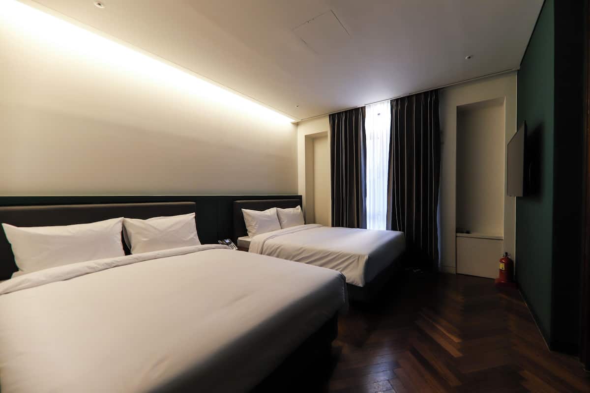 A hotel room with two beds, a flat-screen TV, a telephone, and a fire extinguisher.