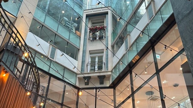 Un atrium moderne doté d’un plafond en verre, de lambris en bois et de guirlandes lumineuses.
