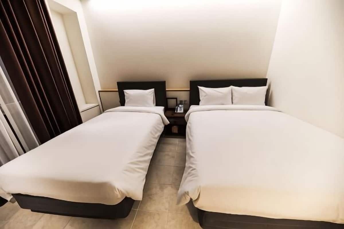 A hotel room with two single beds, a nightstand, and a window with curtains.
