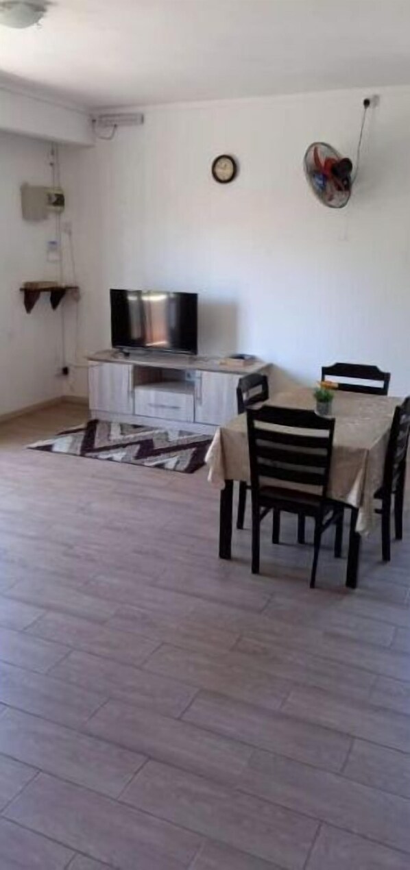 A dining area with a table and chairs, a television on a cabinet, and a patterned rug on the floor.