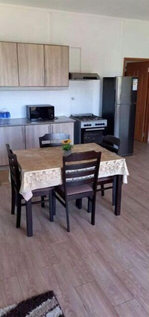 A dining area with a table and chairs, a microwave, a stove, and a refrigerator in the background. - Paisible 9 Chambres à Coucher Stationnement Gratuit Pour les Vacances (Flic en Flac)