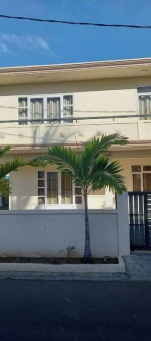 Un edificio de dos pisos con techo plano, un balcón en el nivel superior y una entrada con portón.