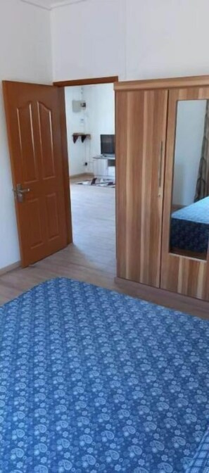 A bedroom with a wooden wardrobe, a patterned blue rug, and a door leading to another room.