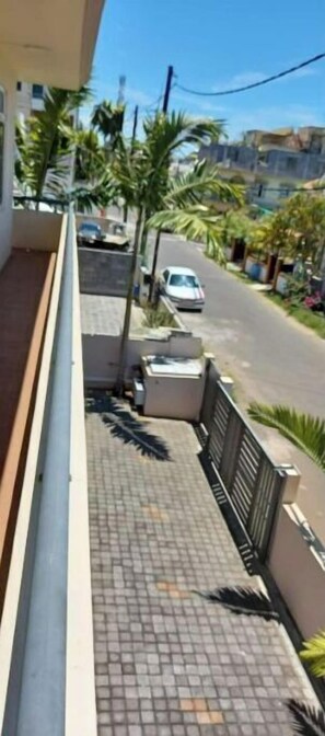 A residential street with a paved sidewalk, a parked car, and palm trees.