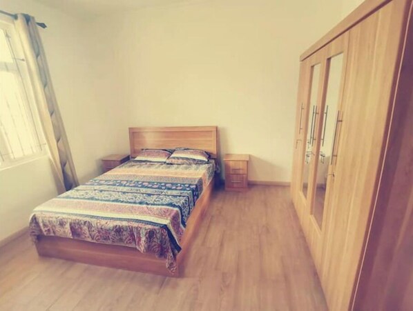 A bedroom with a wooden bed, a nightstand, a wardrobe, and a window with curtains. - Paisible 9 Chambres à Coucher Stationnement Gratuit Pour les Vacances (Flic en Flac)
