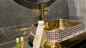 A bathroom with a gold vanity, a round mirror, and two bottles of hand soap on the counter. - Rich Hotel (Mumbai)
