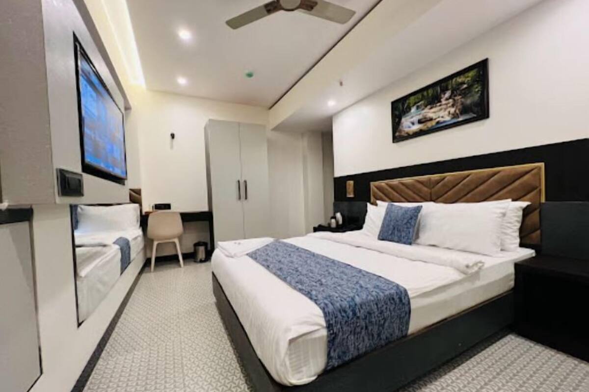 A hotel room with a bed, a desk, a chair, a wardrobe, a ceiling fan, and a painting on the wall.