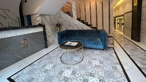 A modern lobby with a marble reception desk, a blue sofa, and a patterned floor. - Rich Hotel (Mumbai)