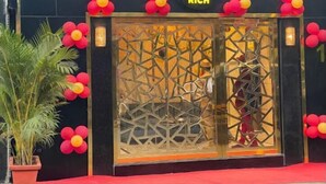A storefront with a black facade, a glass door with a geometric pattern, and red and yellow balloons. - Rich Hotel (Mumbai)