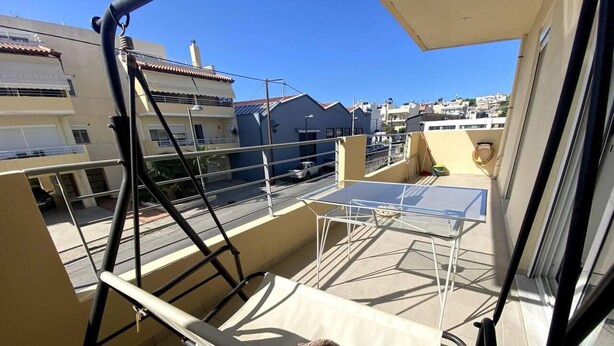 En balkon med en hængestol, et lille bord og udsigt over bybilledet.