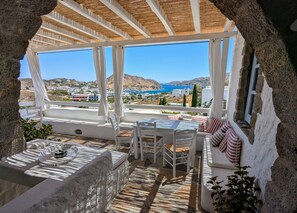 A sunlit terrace with a view of the sea and hills, featuring a table, chairs, and a sofa. - Property with 2 charming Patmos style family homes (Patmos)