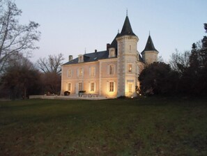 Stately building with a central tower and two smaller towers, set amidst a well-manicured lawn.
