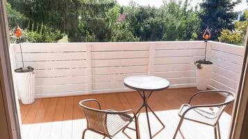 Ein Balkon mit Holzboden, weißer Reling und zwei Korbstühlen um einen kleinen runden Tisch.