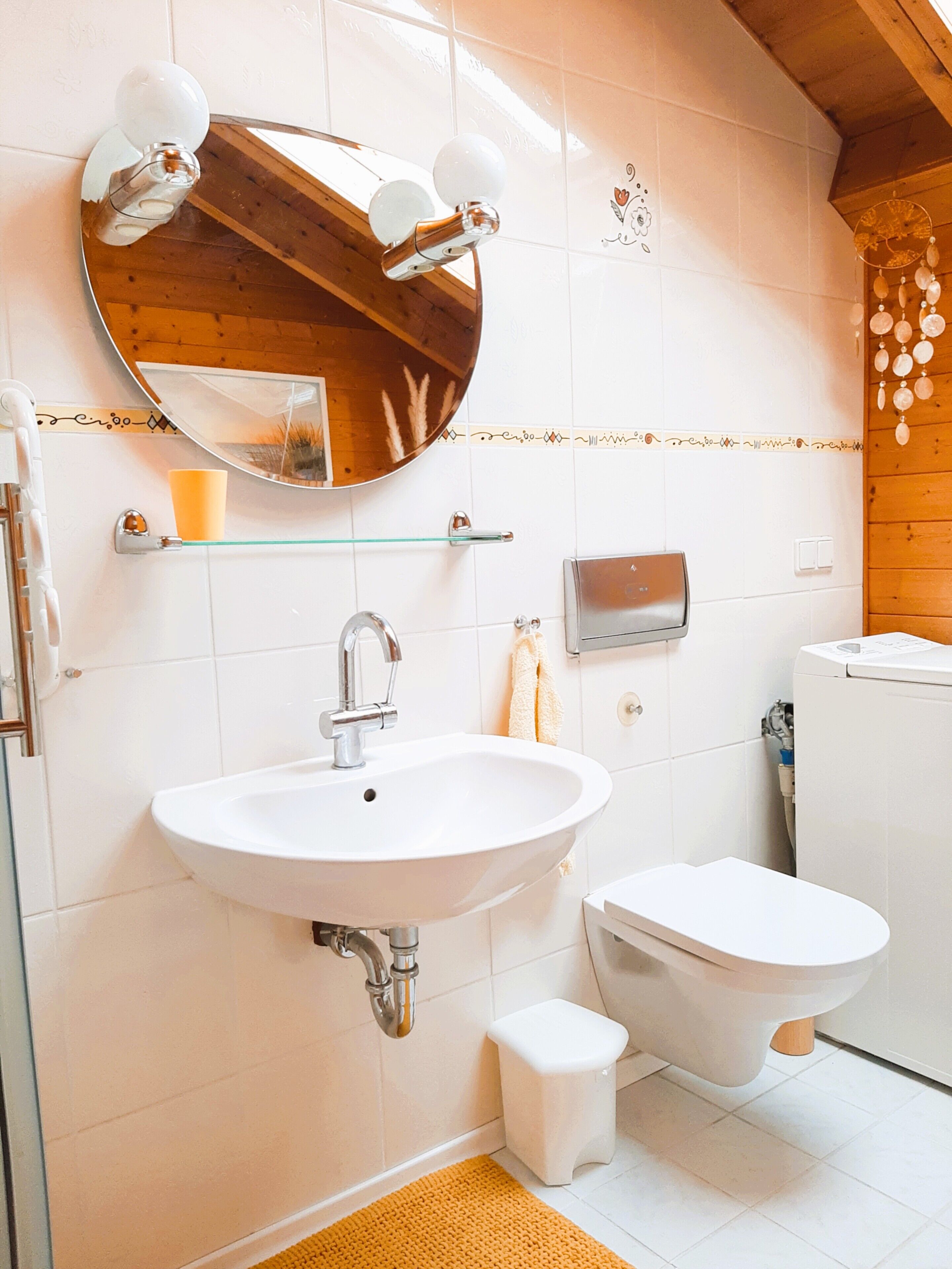 A bathroom with a white sink, a round mirror, a toilet, and a small stool.