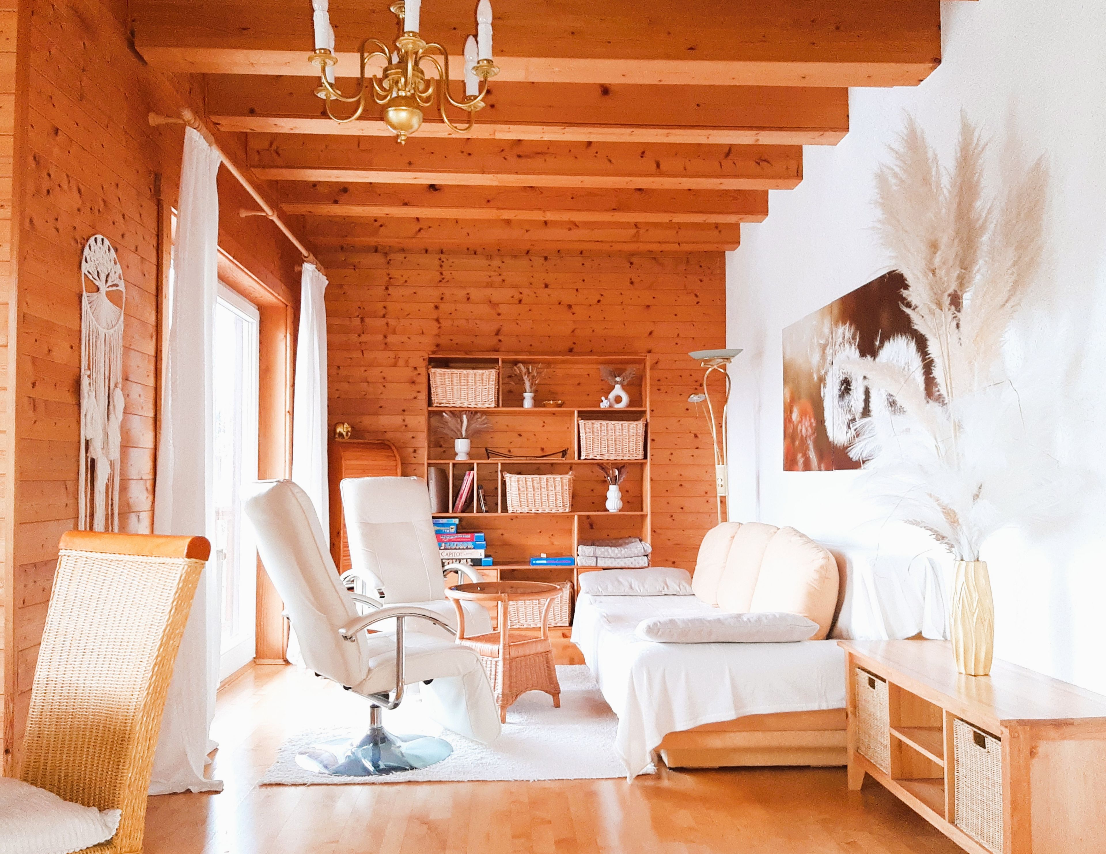 Una habitación acogedora con paredes de madera, un sofá blanco, un sillón blanco, una mesita pequeña y una estantería.
