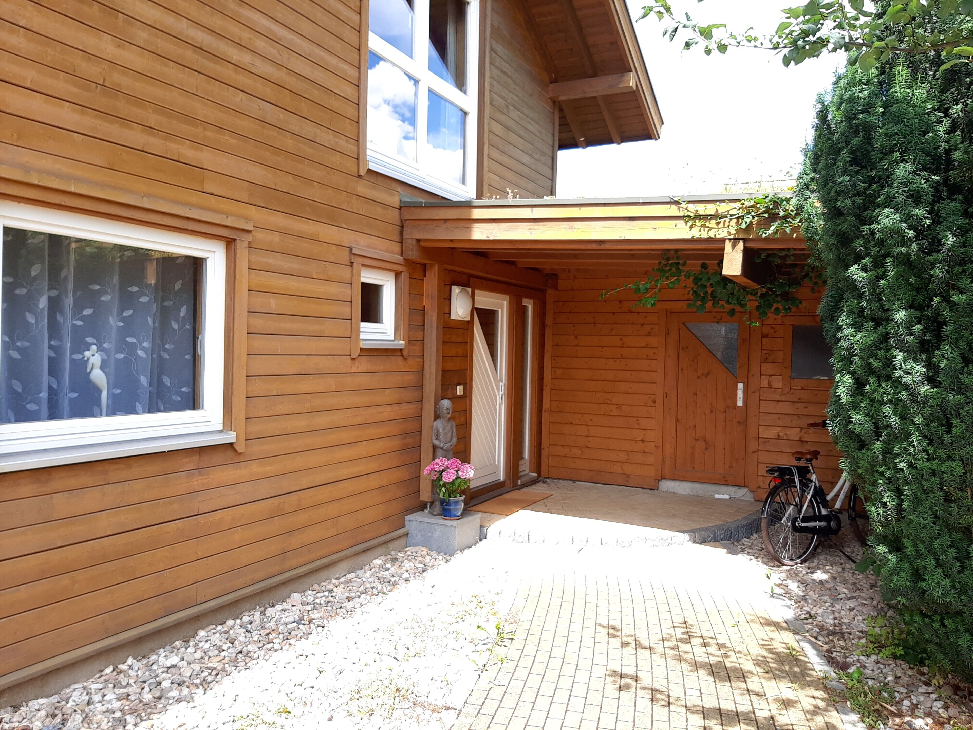 Ein Holzhaus mit befestigtem Eingangsbereich, einer Statue und einem Fahrrad davor.