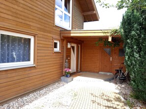 Una casa de fusta amb un vestíbul empedrat, una estàtua i una bicicleta aparcada a l'exterior.