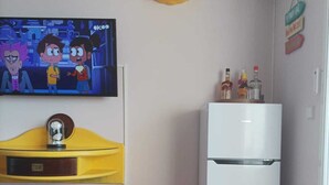 Una cocina compacta con televisor, un armario amarillo, un refrigerador blanco y una pequeña mesa con un adorno.