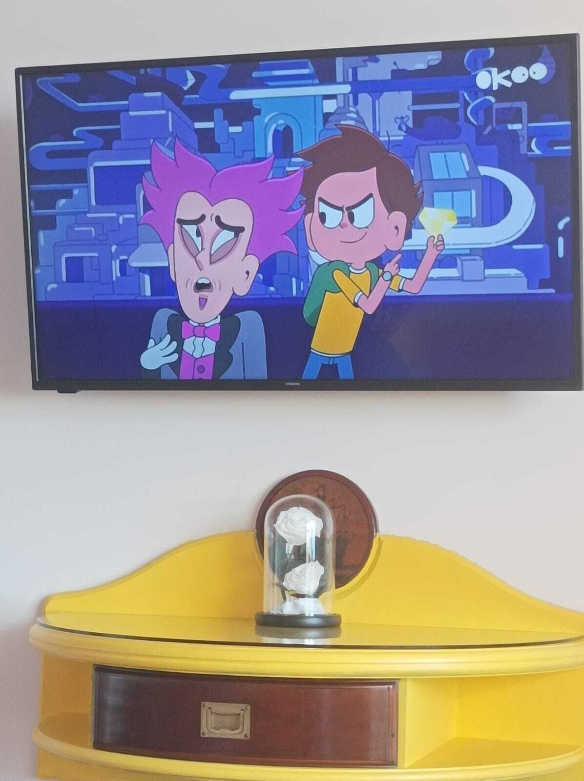 Un televisor mostrando personajes animados, un mueble amarillo con tapa de cristal y una moneda encima.
