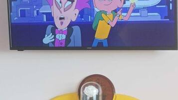 Un televisor mostrando personajes animados, un mueble amarillo con tapa de cristal y una moneda encima.