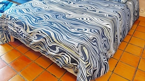 Un dormitorio con cama, sofá azul, un cuadro y una mesita de noche.