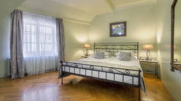 A bedroom with a metal bed frame, two bedside tables with lamps, a large window with sheer curtains, and a framed picture on the wall.