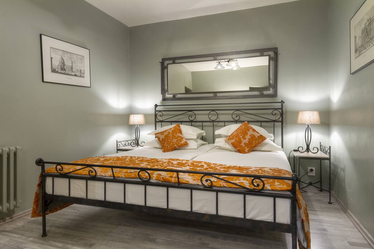 A neatly arranged bedroom with a bed, two bedside tables, a mirror, and a framed picture on the wall.