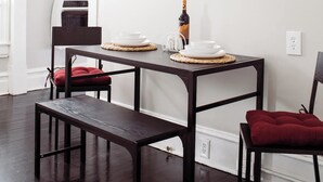 Un comedor con una mesa de madera, dos sillas, un reloj de pared y una lámpara colgante.