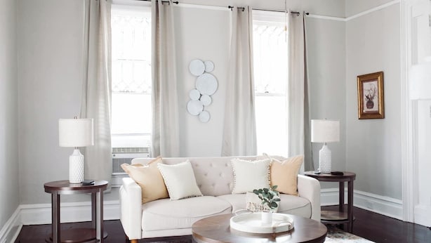 Una sala de estar con un sofá blanco, dos mesas auxiliares con lámparas, una mesa redonda de centro y un elemento decorativo en la pared.