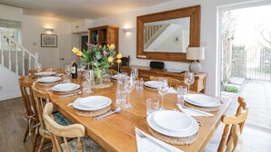 Uma sala de jantar com uma longa mesa de madeira posta para refeição, um espelho acima da mesa e vista para o exterior.