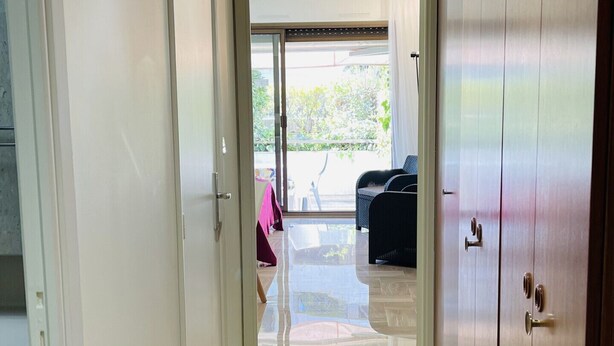 A hallway with a wooden wardrobe, a sliding glass door leading to an outdoor area with furniture. - ROU503 (Cannes)