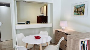 A modern room with a white table, white chairs, a small red object on the table, a lamp, a mirror, and a painting on the wall.