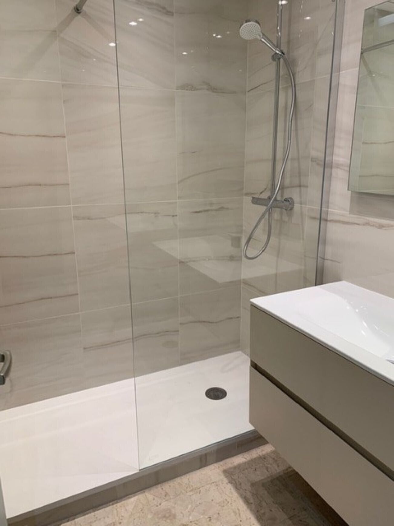 Een moderne badkamer met een glazen douchecabine, een witte wastafel en een vloer van marmer.