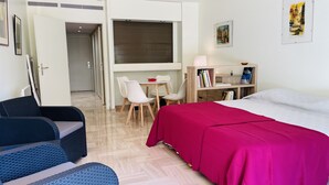 A room with a bed, a desk, two chairs, a bookshelf, and a door leading to another room. - ROU503 (Cannes)
