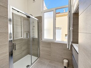 A modern bathroom with a glass-enclosed shower, a window, and a toilet.