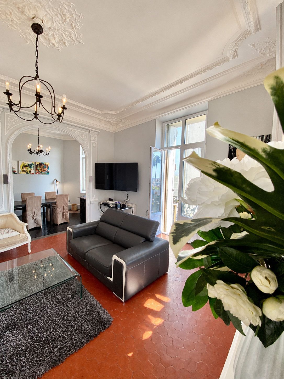 A modern living room with a black sofa, a glass coffee table, and a large plant.
