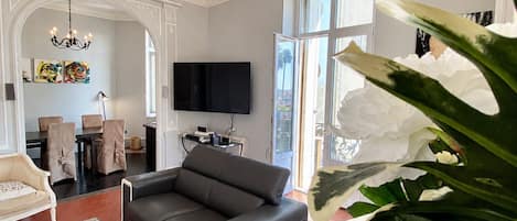 A modern living room with a black sofa, a glass coffee table, and a large plant.