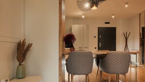 A modern dining area with a wooden table, two grey quilted chairs, a vase with dried plants, and a pendant light. - Nest Inn Scala (Cluj-Napoca)