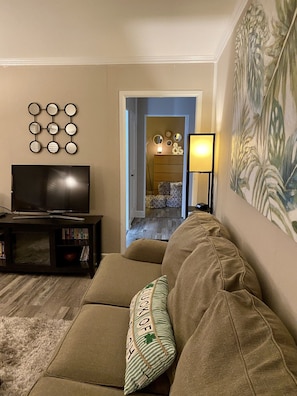 A living room with a sofa, a TV, a bookshelf, a decorative mirror wall, and a door leading to another room.